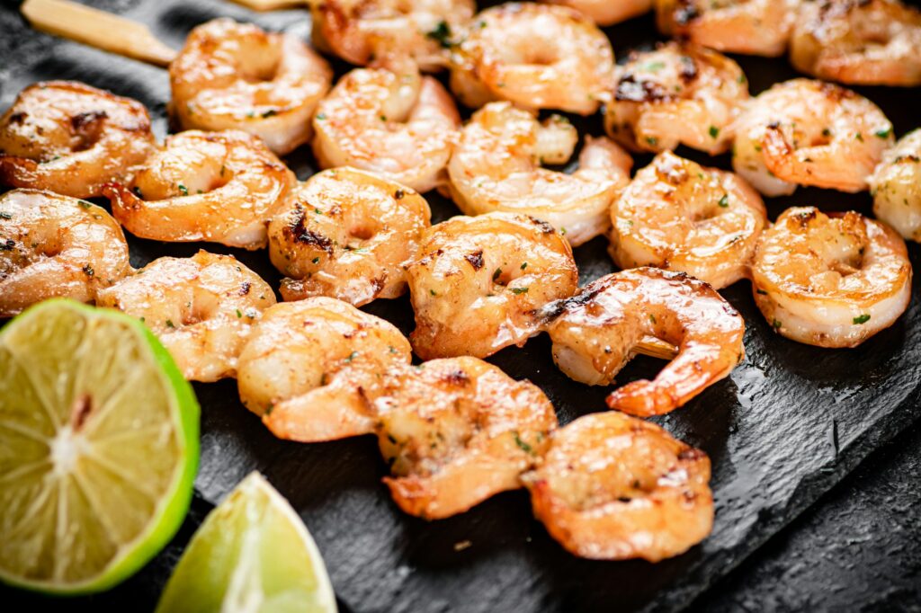 Grilled shrimp on a stone board with pieces of lime.